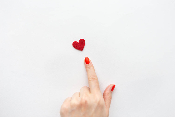 The girl points with her hand to a small red heart. The concept of care and love - Foto, imagen