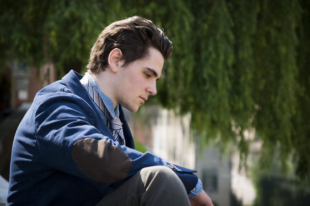 Sad, worried young man sitting outdoor in town - Photo, image