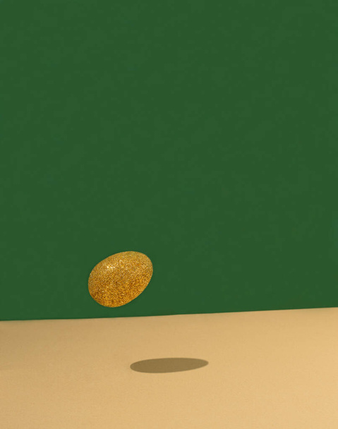 золотое блестящее яйцо на зеленом фоне. Пасхальная концепция. минимальный стиль. - Фото, изображение