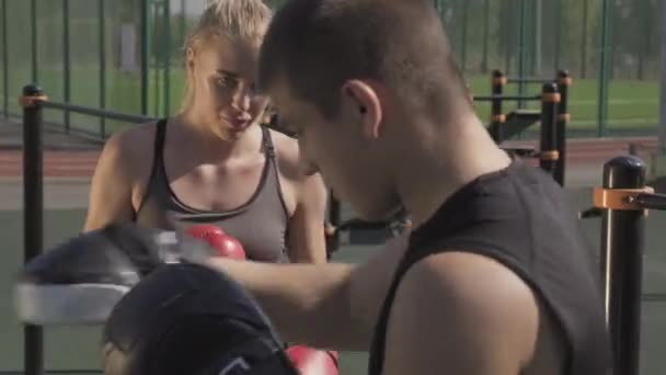 Pas-up záběr mladé sportovní ženy, která má venkovní trénink boxu. Muž trenér ukazuje, jak udeřit a ona opakuje pohyby - Záběry, video