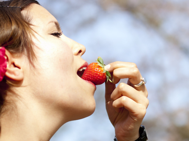 Menina bonita comendo um morango durante um piquenique na primavera
 - Foto, Imagem