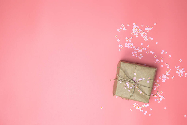Geschenkkarton mit braunem Kraftpapier umgeben von rosa Gänseblümchen und flachem rosa Hintergrund, Frühling, Happy Mothers Day, Valentinstag und anderen Holliday-Konzepten von oben, Modernes Design - Foto, Bild