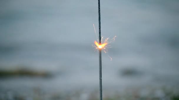 Бенгальский огонь с искрами горит на фоне волн - Кадры, видео