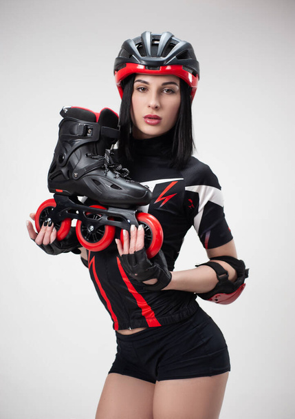 スレンダーな女性でスポーツウェアとヘルメットで彼女の手の中に白い背景にローラースケート - 写真・画像