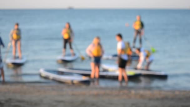 Blurred background. Many people standing and sitting swim on sup boards - Footage, Video