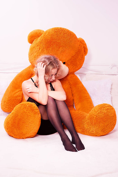 Sad young girl sitting in the hugs of a huge teddy bear on the bed isolated on white background. - Photo, Image
