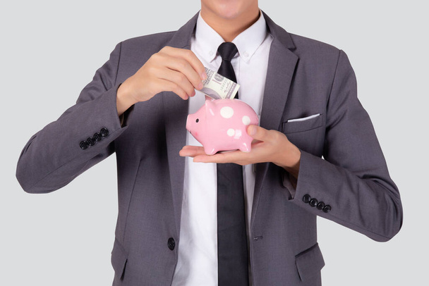 Mladý asijský podnikatel v obleku peníze dolar s prasátko banka izolované na bílém pozadí, obchodní muž spoření s plánovacím rozpočtem a finance pro úspěšné investice a finanční. - Fotografie, Obrázek