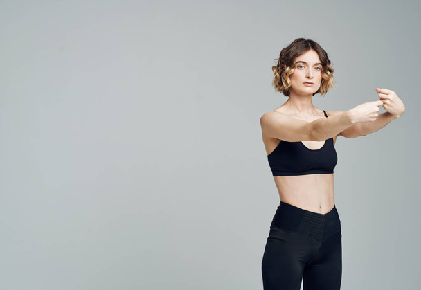 Женщина в темной спортивной одежде на сером фоне жестикулирует руками - Фото, изображение