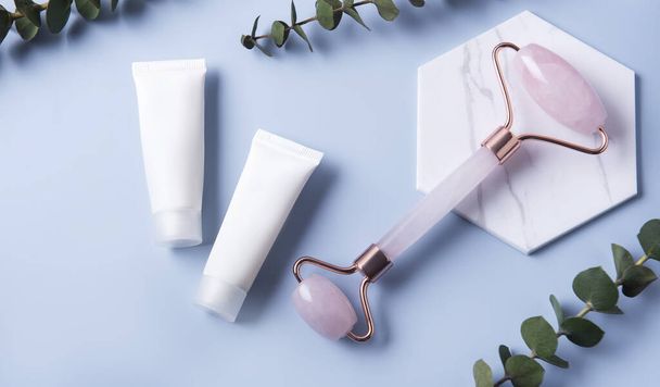 Productos cosméticos, tubos de crema y rodillo facial sobre fondo azul - Foto, imagen
