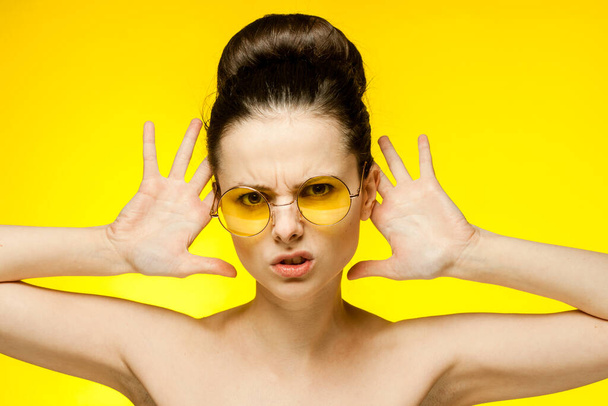 kobieta z gołymi ramionami żółte okulary ręce blisko twarzy przezroczysta skóra - Zdjęcie, obraz