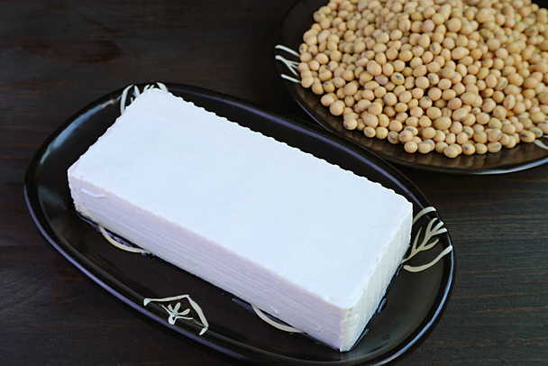 Крупный план мягкого творога из фасоли тофу с размытыми сушеными соевыми бобами на заднем плане - Фото, изображение