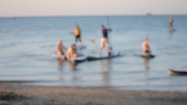 Blurred background. Many people standing and sitting swim on sup boards - Footage, Video