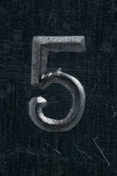 Detailweergave van het getal 5 in reliëf in een grijs en gepolijst metalen plaat.  - Foto, afbeelding