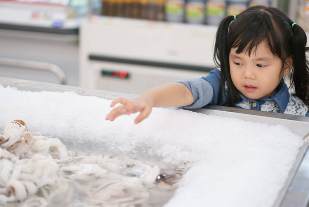 Азійські діти, мила чи маленька дівчинка, забавно вибирають свіжих кальмарів в лотереї для продажу морепродуктів або купують і купують продукти для холестерину в супермаркеті в універмазі. - Фото, зображення