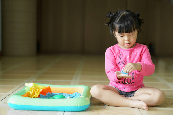 Asian children cute or kid girl wearing pink shirt playing amazing blue sand mold with plastic toy for enjoying and learning at home or nursery with space - Photo, Image