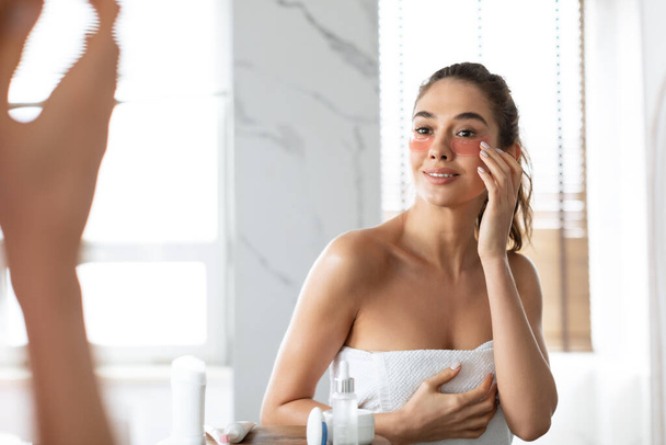Nainen soveltamalla alle silmän laastaria kosteuttava iho alle silmät kylpyhuoneessa - Valokuva, kuva