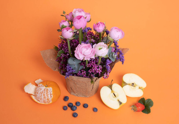 Μπουκέτο με όμορφα ανοιξιάτικα λουλούδια με φρούτα σε πορτοκαλί φόντο. - Φωτογραφία, εικόνα