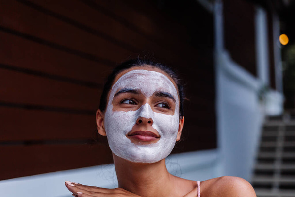 Ritratto esterno di pelle abbronzata calma bella donna caucasica in bikini al centro benessere con maschera peeling bianco sul viso - Foto, immagini