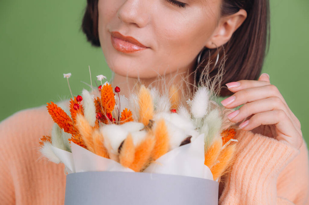 Mujer joven en suéter de melocotón casual aislado sobre fondo verde oliva mantenga naranja caja de flores blanca composición de flores de algodón, gypsophila, trigo y lagurus para un regalo feliz cara sorprendida - Foto, Imagen