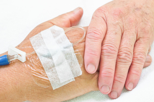 Manos viejas agarrándose unas a otras con solución intravenosa en la mano de un paciente
 - Foto, Imagen