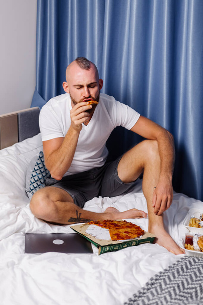 man having fast food at home in bedroom on bed - Foto, imagen