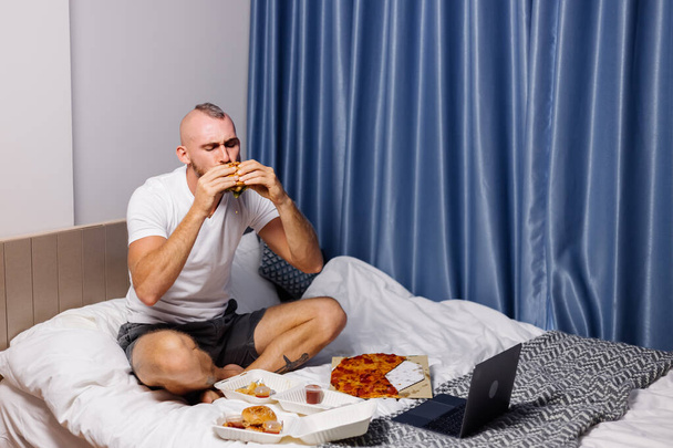 man having fast food at home in bedroom on bed - Фото, изображение