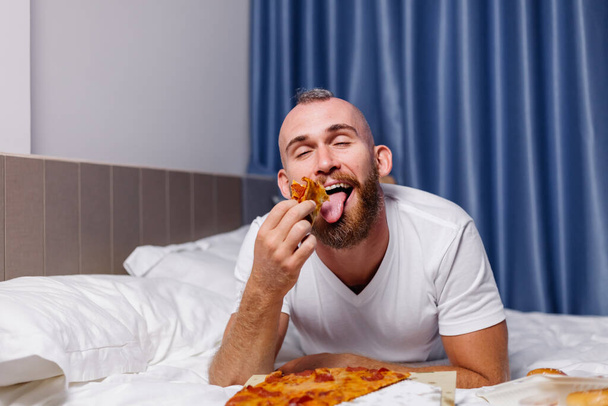άνθρωπος που έχει fast food στο σπίτι στην κρεβατοκάμαρα στο κρεβάτι - Φωτογραφία, εικόνα