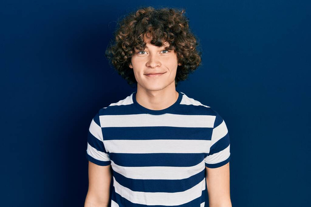 Hombre joven guapo que usa una camiseta de rayas casuales con una sonrisa feliz y fresca en la cara. persona afortunada.  - Foto, imagen