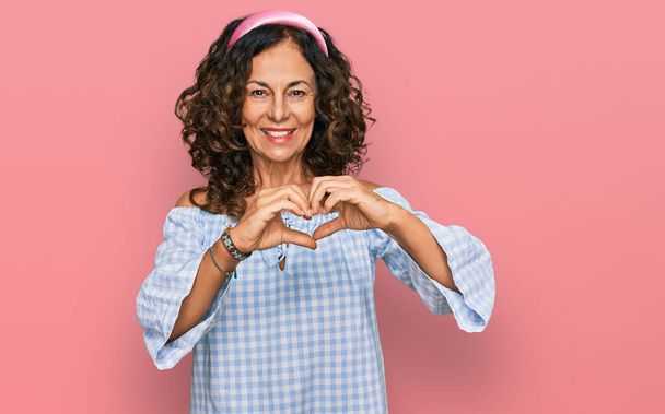 Keski-ikä latino nainen yllään rento vaatteita hymyillen rakastunut osoittaa sydämen symboli ja muoto käsin. romanttinen käsite.  - Valokuva, kuva