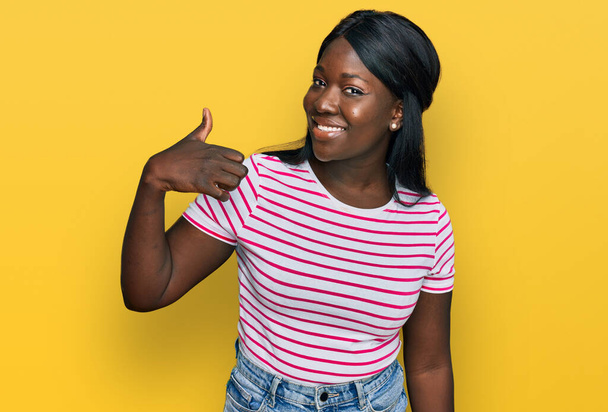 Μια νεαρή Αφρικανή που φοράει ριγέ μπλουζάκι και κάνει χαρούμενη χειρονομία με το χέρι. έγκριση έκφρασης κοιτάζοντας την κάμερα που δείχνει την επιτυχία.  - Φωτογραφία, εικόνα