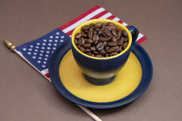 Une tasse de café remplie à ras bord de grains de café torréfiés se dresse sur le drapeau américain. Concept : Café américain, goût riche, exportation et importation d'Amérique. - Photo, image