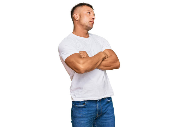 Hombre musculoso guapo con camiseta blanca casual mirando a un lado con los brazos cruzados convencidos y confiados  - Foto, imagen