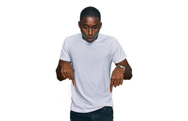 Gündelik beyaz tişört giyen genç Afro-Amerikan bir adam parmaklarını göstererek reklamını yapıyor, şaşırmış bir yüz ve ağzını açıyor.  - Fotoğraf, Görsel
