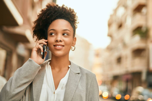 Молодая африканская американская бизнесвумен улыбается счастливо разговаривая по смартфону в городе. - Фото, изображение