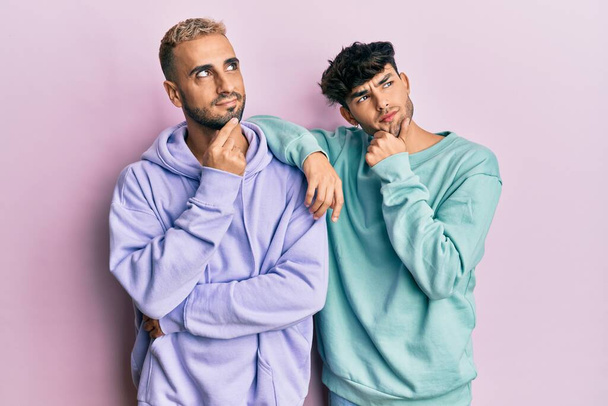 Homosexual gay couple standing together wearing casual clothes with hand on chin thinking about question, pensive expression. smiling and thoughtful face. doubt concept.  - Fotoğraf, Görsel
