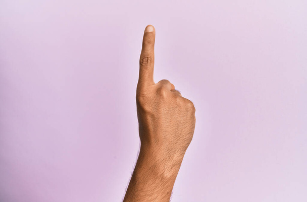 Ramię i ręka białego młodzieńca nad różowym odizolowanym tłem licząc numer jeden palcem wskazującym, pokazując ideę i zrozumienie  - Zdjęcie, obraz