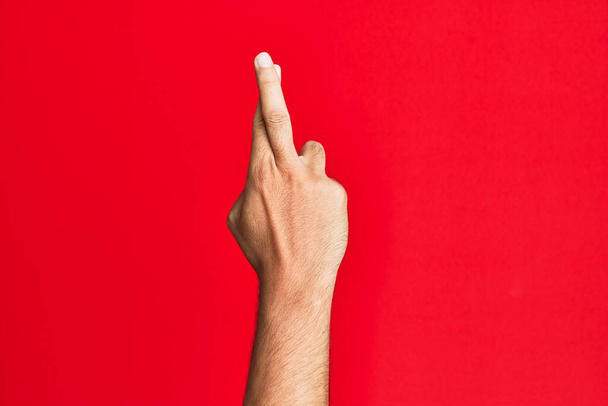 Arm of caucasian white young man over red isolated background gesturing fingers crossed, superstition and lucky gesture, lucky and hope expression  - Foto, Imagem