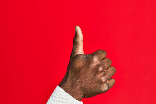 Arm en hand van Afro-Amerikaanse zwarte jongeman over rood geïsoleerde achtergrond doet succesvolle goedkeuring gebaar met duimen omhoog, validatie en positief symbool  - Foto, afbeelding