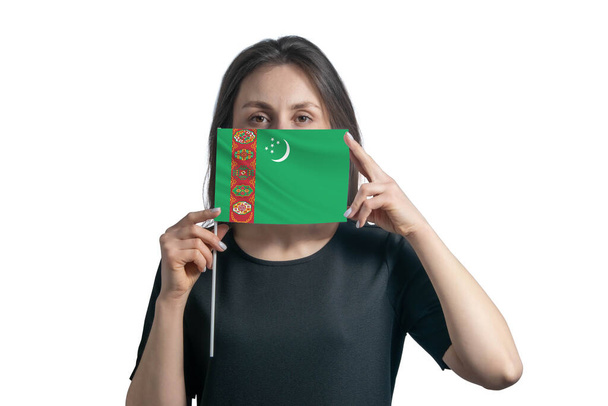 幸せな若い白人女性は旗を持っているトルクメニスタンの国旗を持ち、白い背景にそれで彼女の顔を覆います. - 写真・画像