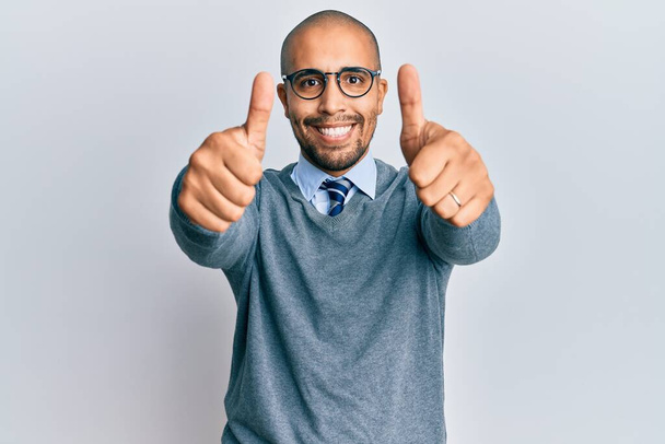 Hispanic adult man wearing glasses and business style approving doing positive gesture with hand, thumbs up smiling and happy for success. winner gesture.  - Photo, Image