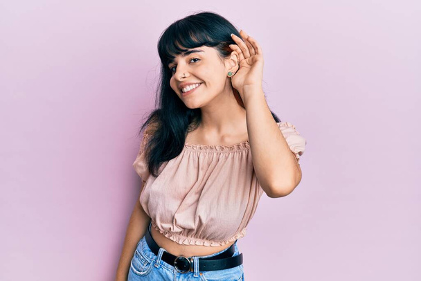 Young hispanic girl wearing casual clothes smiling with hand over ear listening an hearing to rumor or gossip. deafness concept.  - Foto, immagini