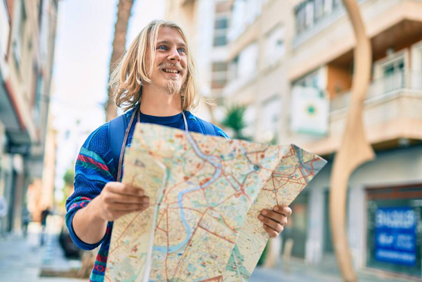 Joven turista escandinavo sonriendo feliz usando mapa en la ciudad. - Foto, Imagen
