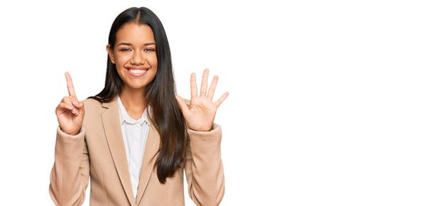 Krásná hispánská žena v obchodní bundě ukazuje a ukazuje prsty číslo šest a zároveň se usmívá sebevědomě a šťastně.  - Fotografie, Obrázek