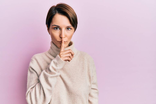 Young brunette woman with short hair wearing casual winter sweater asking to be quiet with finger on lips. silence and secret concept.  - Valokuva, kuva