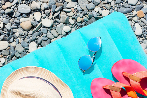 Nyári utazási tartozékok, mint a napsapka, kerek tükör napszemüveg, rózsaszín flip papucs fekszik fényes úszómatrac szürke kerek tengeri kövek. Tengerparti nyaralás előkészítése.  - Fotó, kép