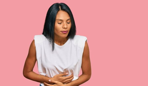 若いアフリカ系アメリカ人女性が胃の上に手でカジュアルな服を着ているのは、消化不良、痛みを伴う病気が具合が悪いからです。キャッシュ・コンセプト.  - 写真・画像