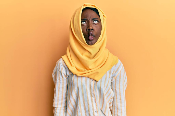 Красивая африканская молодая женщина в традиционном исламском шарфе хиджаба делает рыбное лицо с губами, сумасшедший и смешной жест. Смешное выражение.  - Фото, изображение