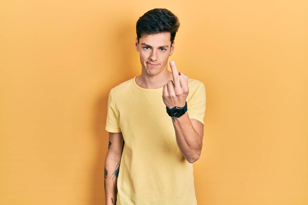 junger hispanischer Mann in lässigem gelben T-Shirt mit Mittelfinger, unhöflichem und unhöflichem Gesichtsausdruck  - Foto, Bild