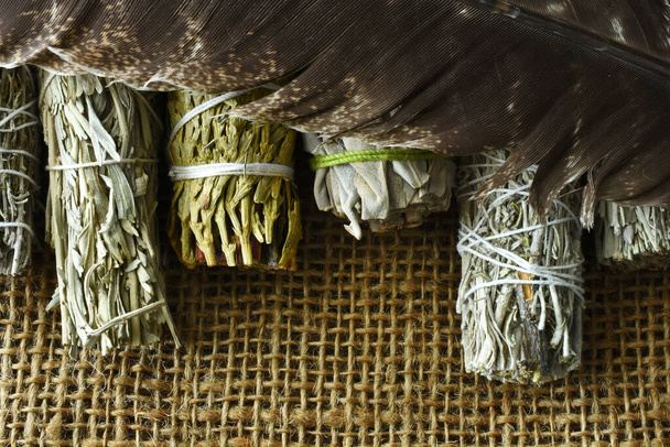 Una imagen de vista superior de una variedad de paquetes de manchas curativas con plumas sagradas en la arpillera.  - Foto, Imagen