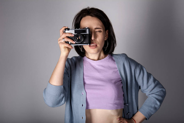 Een jong meisje in een trui en een top poseert met een vintage film camera op een lichte achtergrond. - Foto, afbeelding